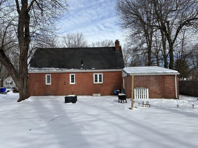 snow covered house featuring a chimney and brick siding