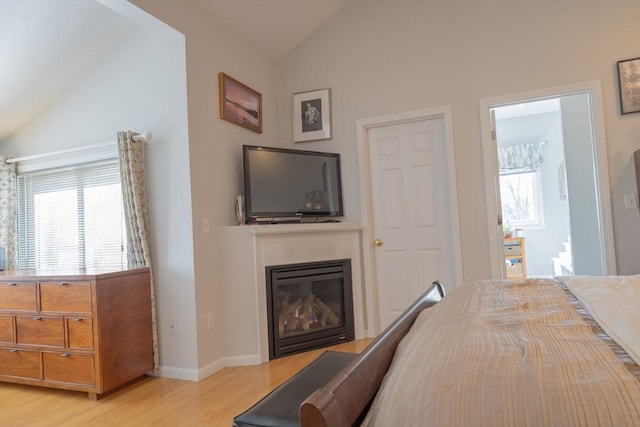 bedroom featuring vaulted ceiling, multiple windows, a glass covered fireplace, and light wood-style flooring