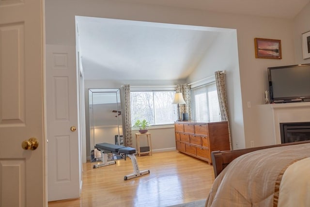 bedroom featuring lofted ceiling, light wood-style flooring, and a glass covered fireplace