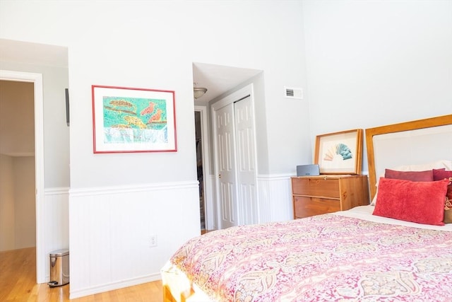 bedroom with light wood finished floors, visible vents, a closet, and wainscoting