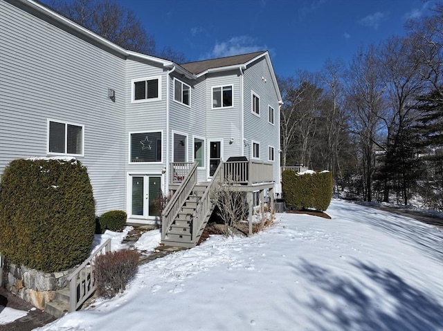 snow covered back of property featuring stairs and a wooden deck