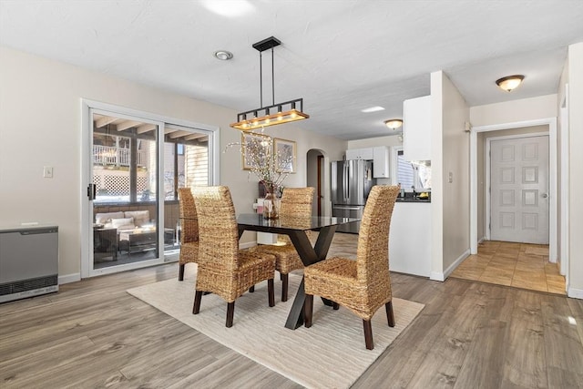 dining room with arched walkways, light wood finished floors, heating unit, and baseboards