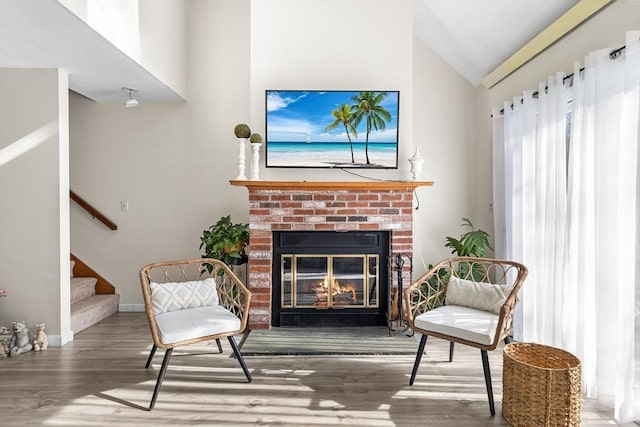 sitting room with lofted ceiling, wood finished floors, baseboards, stairway, and a brick fireplace