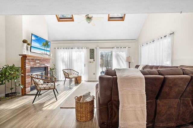 living area with a brick fireplace, vaulted ceiling with skylight, baseboards, and wood finished floors