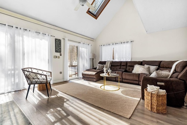 living area featuring ceiling fan, high vaulted ceiling, a skylight, and wood finished floors