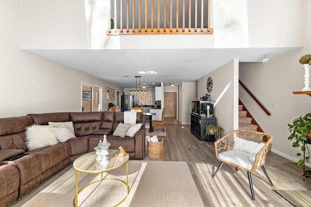 living area featuring stairs, light wood-type flooring, a towering ceiling, and baseboards