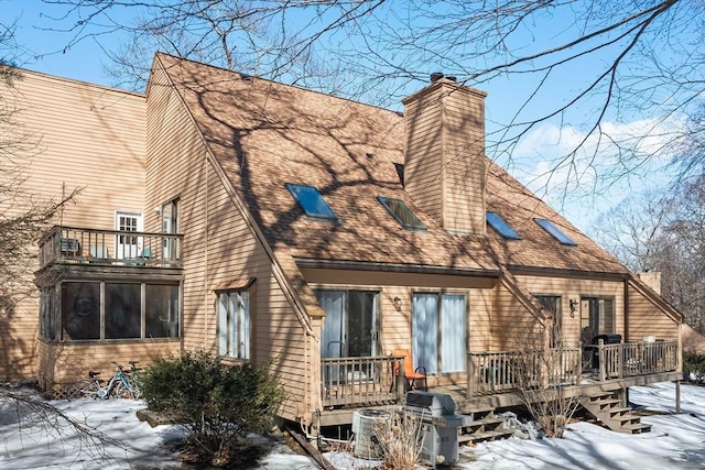 snow covered house featuring a deck, roof with shingles, and a chimney