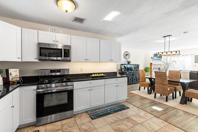 kitchen featuring appliances with stainless steel finishes, dark countertops, visible vents, and white cabinetry