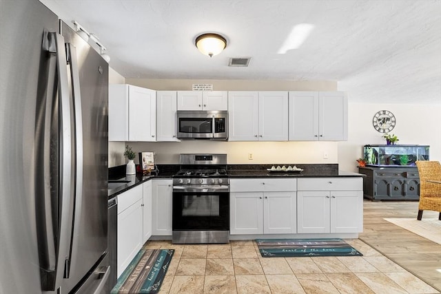 kitchen with stainless steel appliances, dark countertops, visible vents, and white cabinets