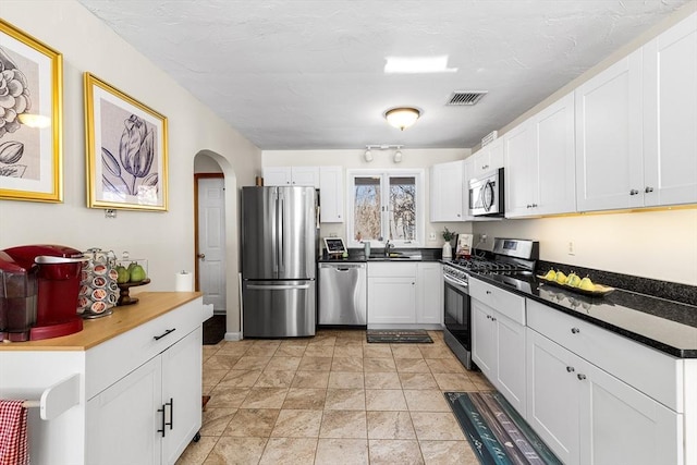 kitchen with visible vents, white cabinets, dark countertops, stainless steel appliances, and a sink