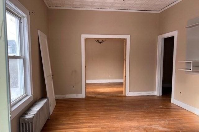 unfurnished room with light wood finished floors, radiator, an ornate ceiling, and baseboards