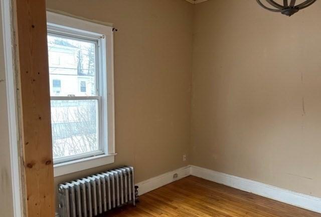 unfurnished room featuring baseboards, radiator, and wood finished floors