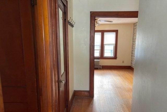 hallway with baseboards, hardwood / wood-style floors, and radiator heating unit