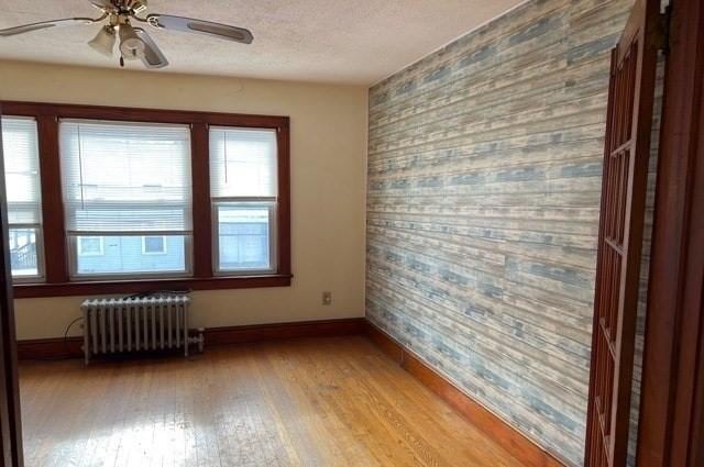 spare room featuring radiator, a ceiling fan, baseboards, light wood-style flooring, and an accent wall