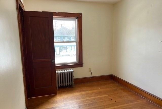 unfurnished room featuring radiator heating unit, light wood-style floors, and baseboards