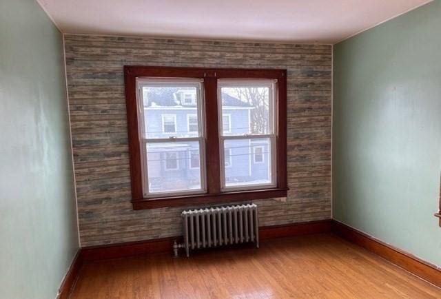 unfurnished room featuring light wood-type flooring, baseboards, and radiator