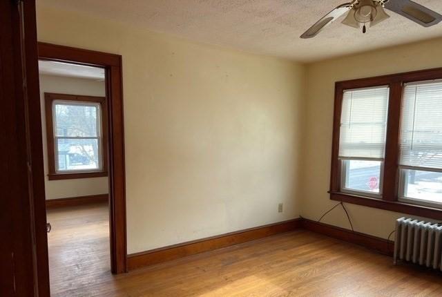 spare room featuring a wealth of natural light, baseboards, radiator, and light wood finished floors