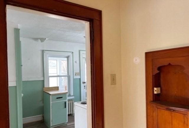 corridor with dark wood-style floors, radiator heating unit, and baseboards