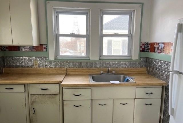 kitchen with light countertops, white cabinets, freestanding refrigerator, and a sink