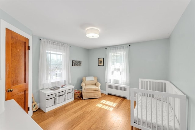 bedroom with light wood-type flooring, radiator, and a crib