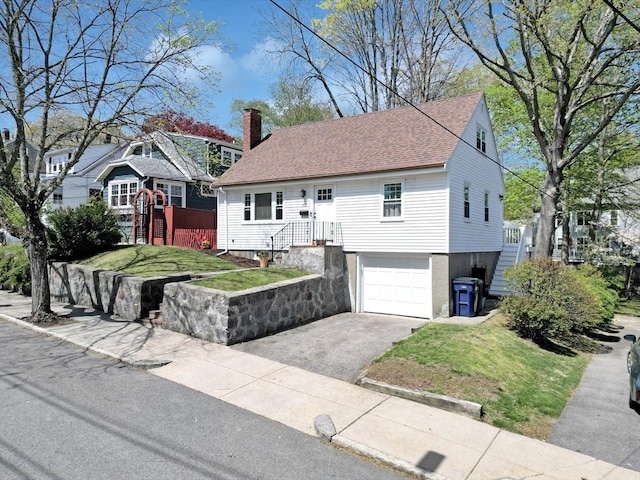 view of front facade featuring driveway, a chimney, a front yard, and a garage