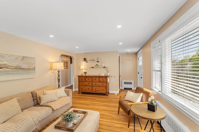 living room with baseboards, radiator heating unit, recessed lighting, arched walkways, and light wood finished floors