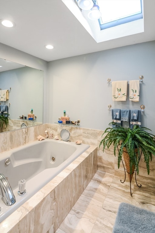 bathroom featuring a skylight and tiled bath