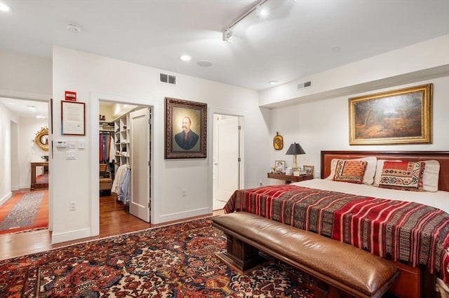 bedroom with a walk in closet, a closet, wood-type flooring, and track lighting