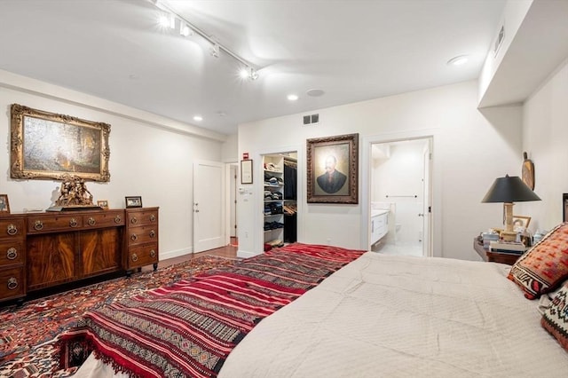 bedroom with rail lighting, a spacious closet, ensuite bath, and a closet