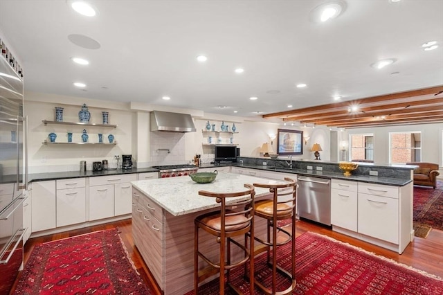 kitchen with wall chimney exhaust hood, stainless steel appliances, a center island, and white cabinets