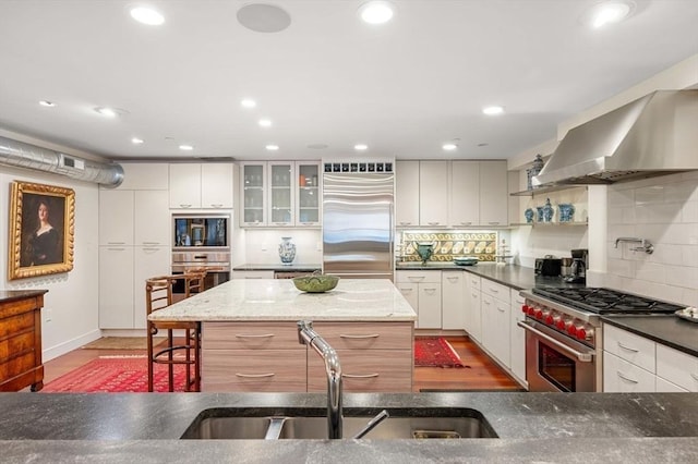 kitchen with high end appliances, a center island, range hood, and white cabinets