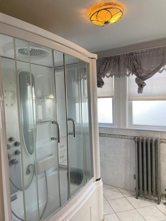 bathroom featuring tile patterned floors, enclosed tub / shower combo, tile walls, and radiator