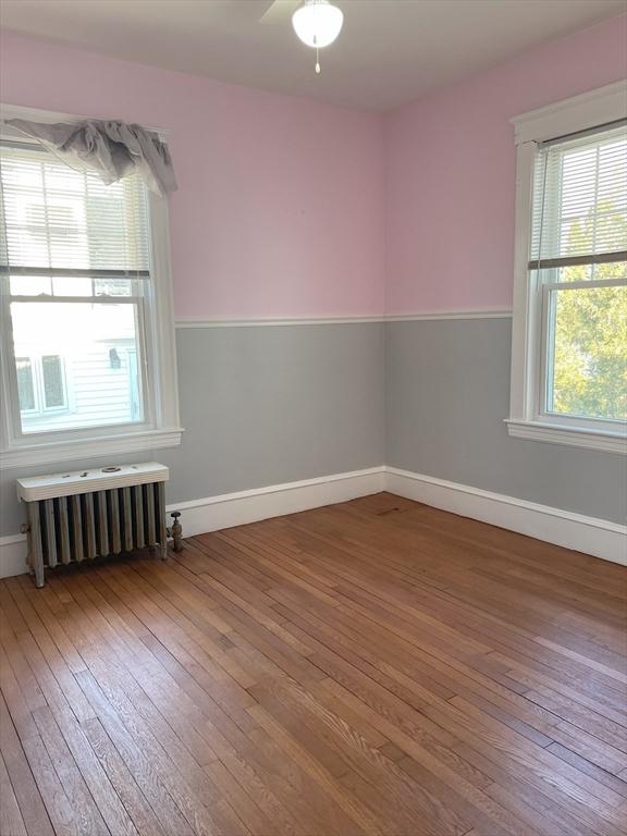 empty room featuring hardwood / wood-style floors, radiator, and ceiling fan