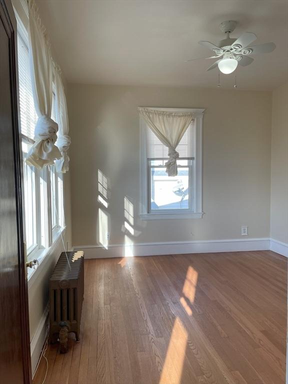 empty room with ceiling fan, wood-type flooring, and radiator