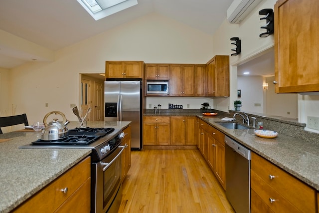 kitchen featuring light stone counters, an AC wall unit, sink, light hardwood / wood-style floors, and stainless steel appliances