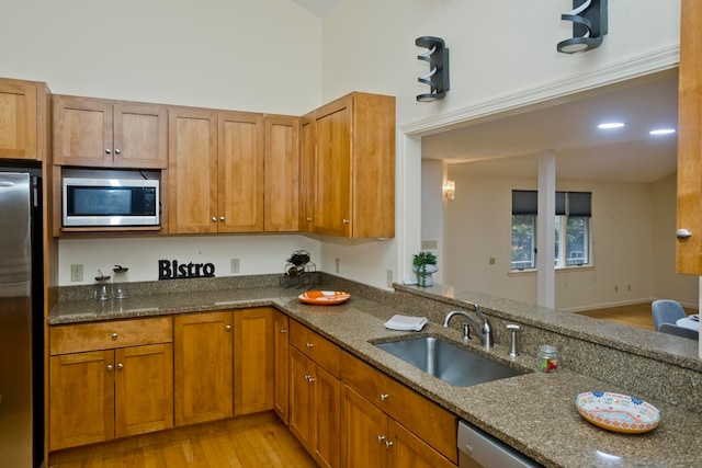 kitchen featuring kitchen peninsula, stainless steel appliances, dark stone counters, sink, and light wood-type flooring