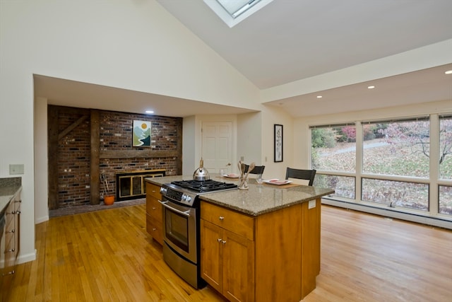 kitchen with light stone countertops, light wood-type flooring, a skylight, stainless steel range with gas cooktop, and a center island