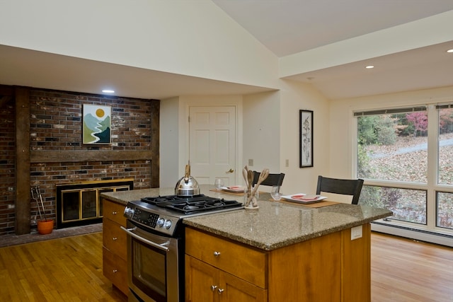 kitchen with vaulted ceiling, stainless steel gas stove, light hardwood / wood-style flooring, and a fireplace