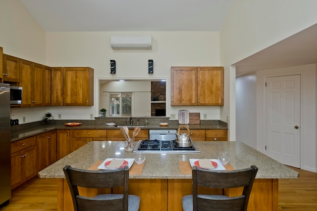 kitchen featuring a wall unit AC, appliances with stainless steel finishes, a kitchen bar, light wood-type flooring, and a center island