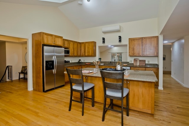 kitchen featuring an AC wall unit, a kitchen breakfast bar, light hardwood / wood-style flooring, a center island, and appliances with stainless steel finishes