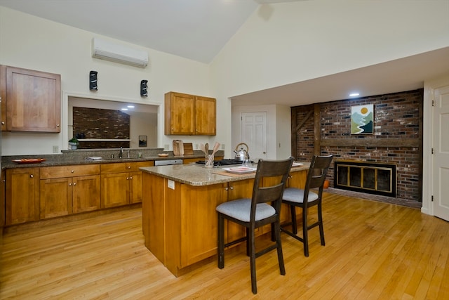 kitchen featuring light wood-type flooring, a kitchen bar, a wall mounted air conditioner, a brick fireplace, and a kitchen island with sink