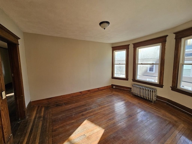 empty room with dark hardwood / wood-style flooring and radiator heating unit