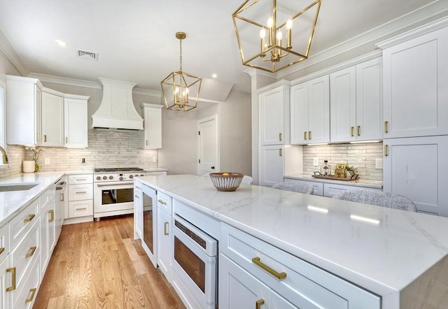 46 Pearl St, Melrose, MA 02176 - kitchen with premium range hood, white gas range oven, a chandelier, tasteful backsplash, and white cabinets