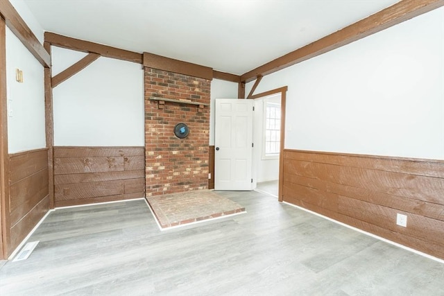 spare room with wooden walls, beamed ceiling, a wainscoted wall, and wood finished floors