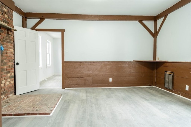unfurnished room with beam ceiling, a wainscoted wall, and wood finished floors