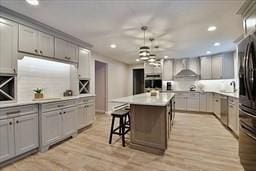 kitchen with wall chimney exhaust hood, gray cabinets, freestanding refrigerator, and a center island