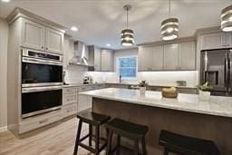 kitchen with appliances with stainless steel finishes, light countertops, wall chimney range hood, a kitchen bar, and pendant lighting