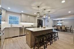 kitchen with a breakfast bar area, a kitchen island with sink, light wood-style flooring, a sink, and stainless steel dishwasher