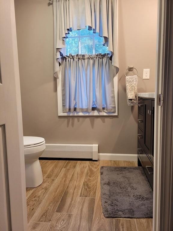 bathroom featuring baseboards, toilet, wood finished floors, vanity, and a baseboard heating unit