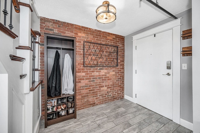 foyer with brick wall, light hardwood / wood-style flooring, and a textured ceiling